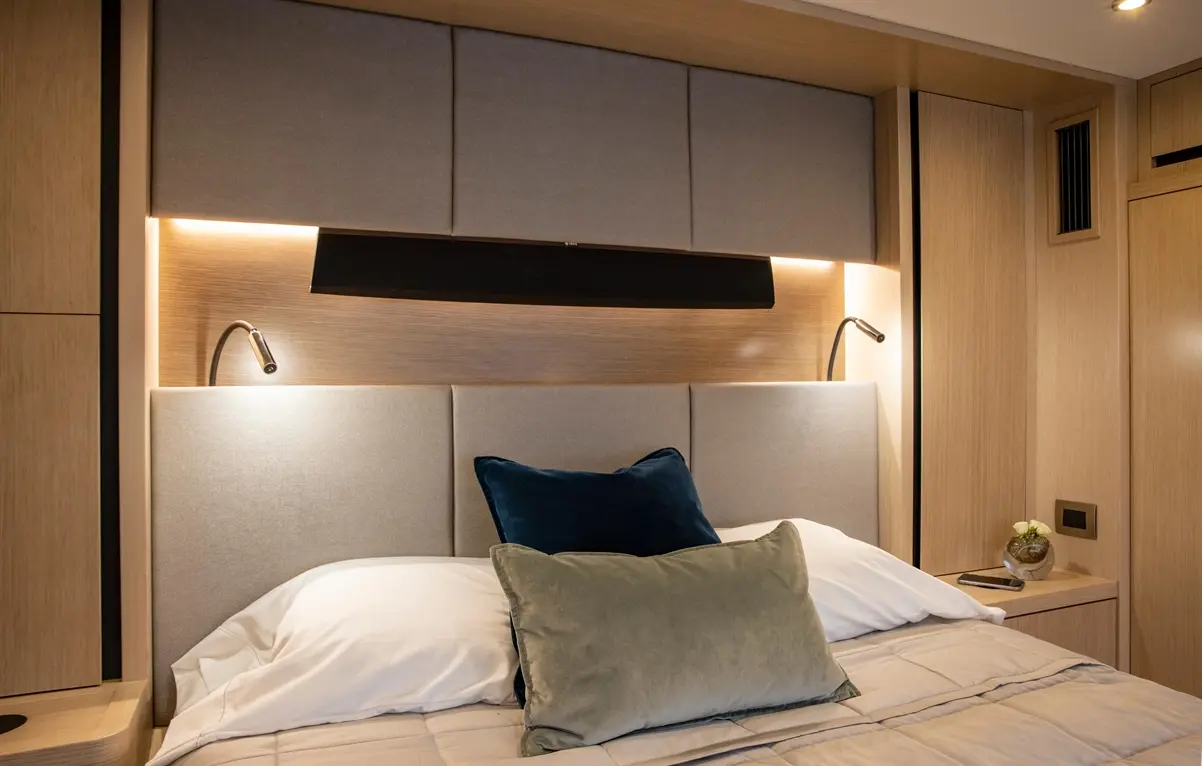 Modern bedroom featuring a grey upholstered headboard, decorative pillows, bedside lamp, and a small plant on a dresser.